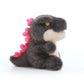 kaiju baby plush toy with a cream belly and pink back spikes, shown from the side.