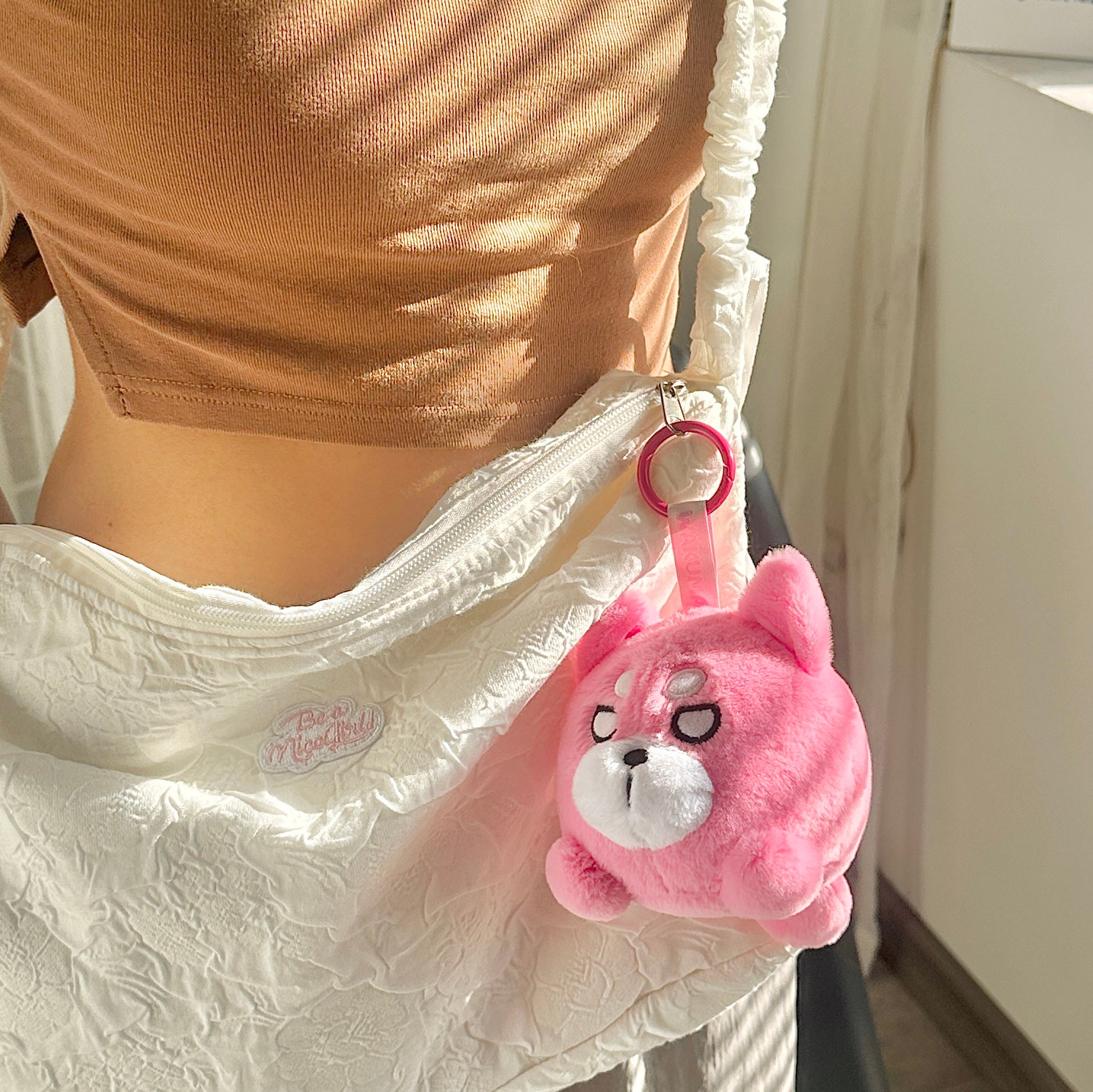Pink round Wakuma bear plush keychain on bag zipper.